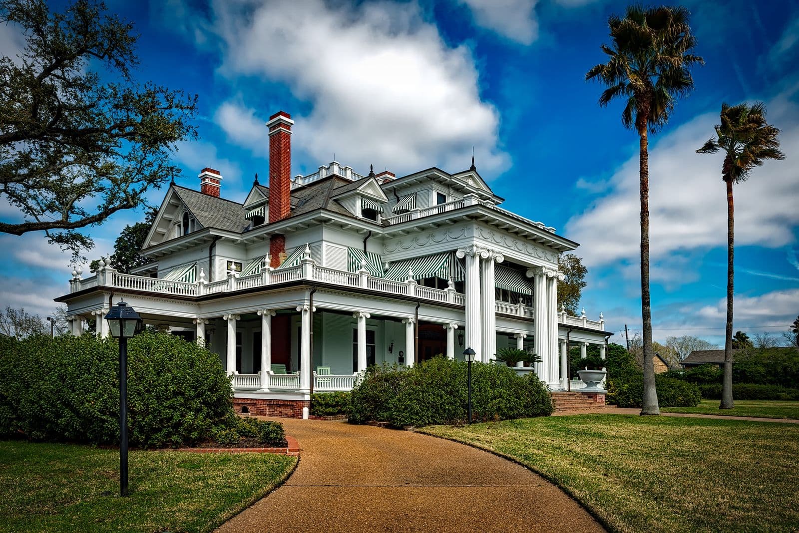 A white building with columns and palm trees under a blue sky.